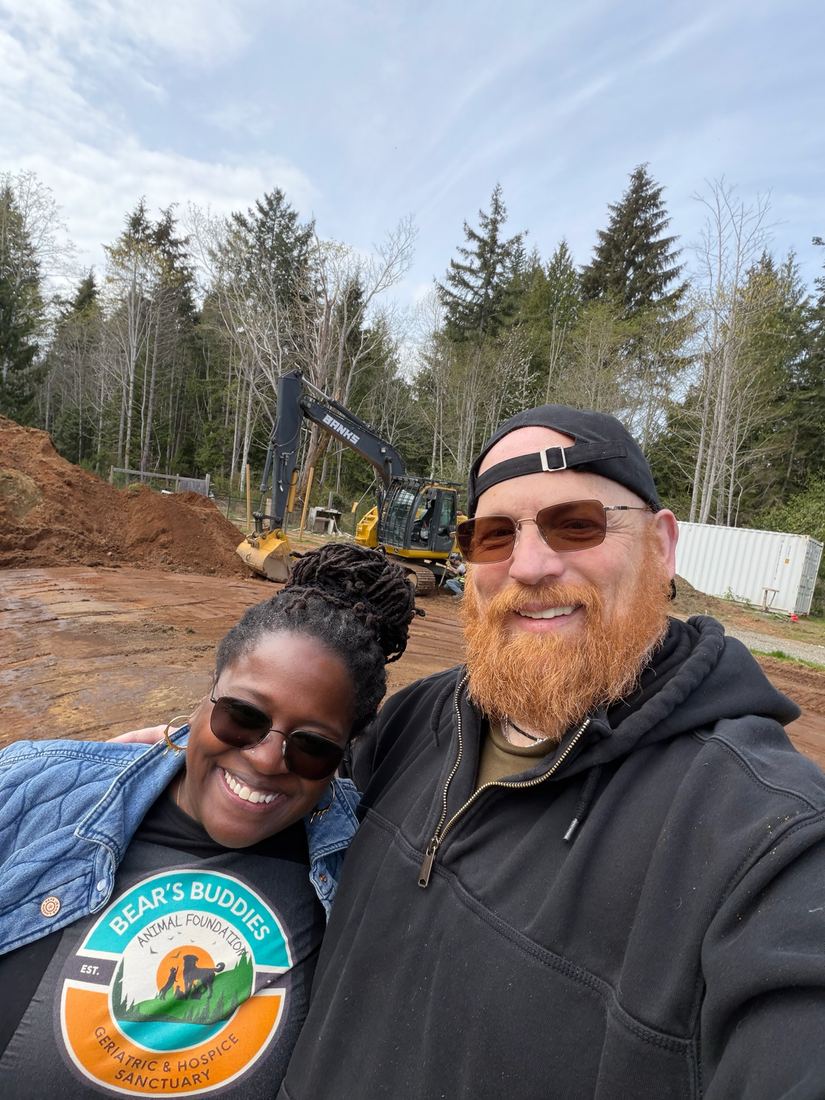 Kimberly and Keith on the cleared ground with an excavator working behind them
